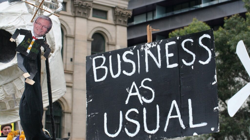 Banner in a protest displaying the text "Business as usual".