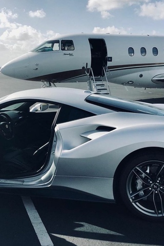An expensive sports car in the foreground with a private jet in the background.